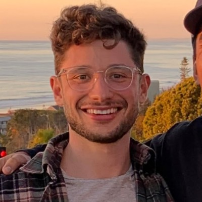 Zach smiling outdoors in the evening, with the ocean behind him